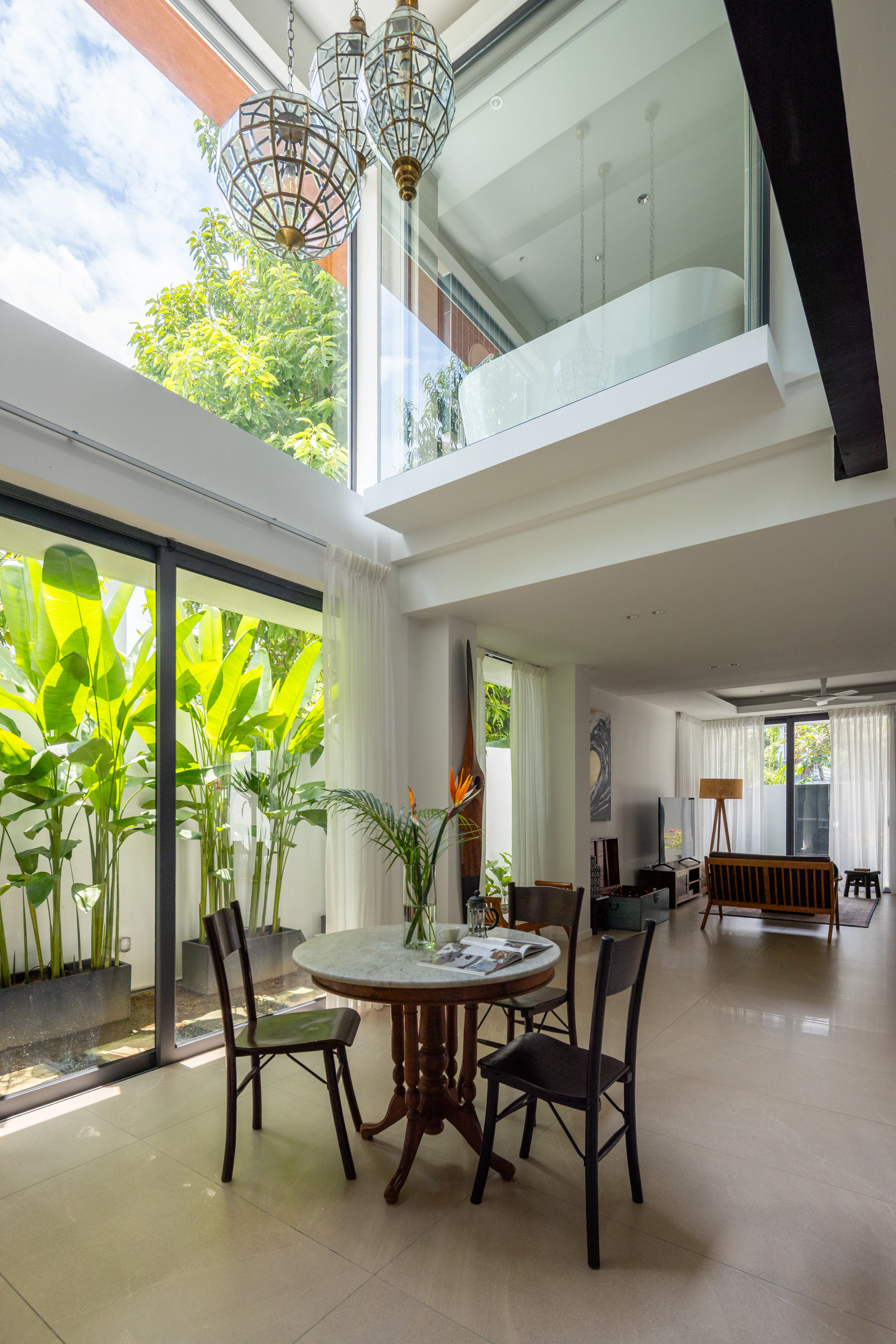 Double-height interior with pendant lights, greenery and a glazed upper floor